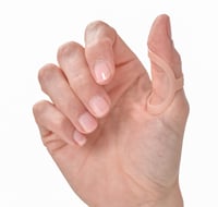 Close-up of a hand with a nude-toned Oval-8 splint supporting the thumb joint, designed to prevent catching and locking caused by trigger thumb.